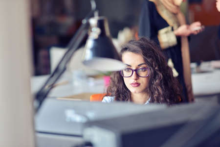Portrait of smiling pretty young business woman in glasses sitting on workplaceの写真素材