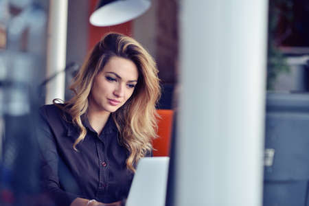 Portrait of smiling pretty young business woman sitting on workplaceの写真素材