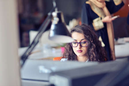 Portrait of smiling pretty young business woman in glasses sitting on workplaceの写真素材