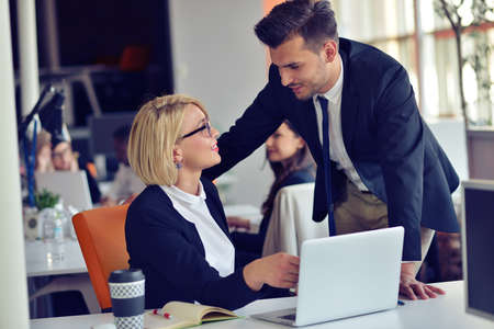 Beautiful young business partners are using a laptop, discussing documents and smiling while working in office.の写真素材