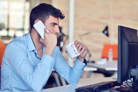 Businessman relaxing with legs up on desk, drinking coffee while dreaming about future at workplace in modern office.の写真素材