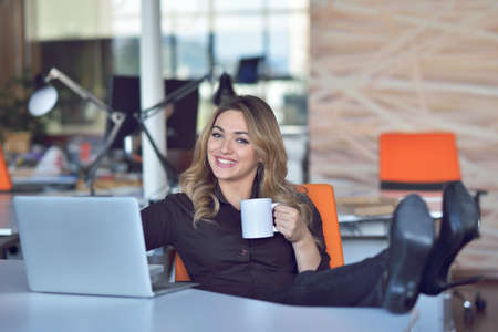 Happy beautiful young business woman sitting and talking on cell phone in officeの写真素材