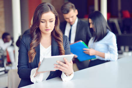Confident attractive young business woman with tablet in hands in modern office start up office