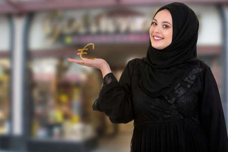 studio shot of young woman wearing traditional arabic clothing. shes holding pound symbol in hand.