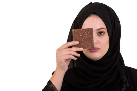 Lovely smiling muslim woman with hijab eating chocolate isolated on white background.
