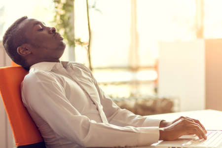 Overworking african-american employee in office. Tired and having headache while working on a new projectの写真素材