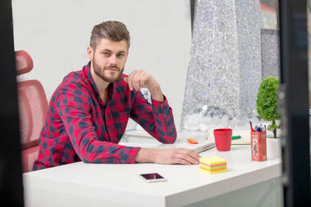 Concentrated on work. Concentrated young beard man working on laptop while sitting at his working place in officeの写真素材