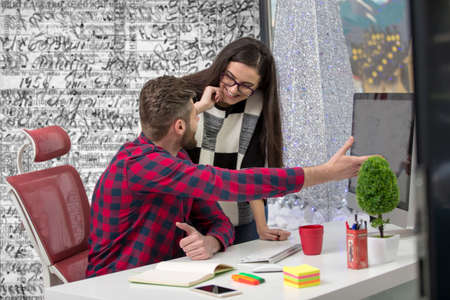 Couple of young designers working at modern office, two coworkers discussing fun project over a...