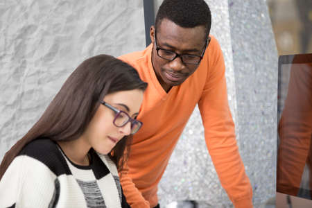 Two diverse work colleagues smiling and writing down notes while sitting together at a table in a modern officeの写真素材