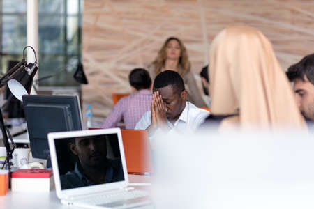 Frustrated young african entrepreneur with sad grimace in front of his laptop in officeの写真素材
