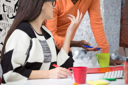 Two diverse work colleagues smiling and writing down notes while sitting together at a table in a modern officeの写真素材