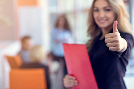 Business woman with folders standing and team mates working in meeting room at office.