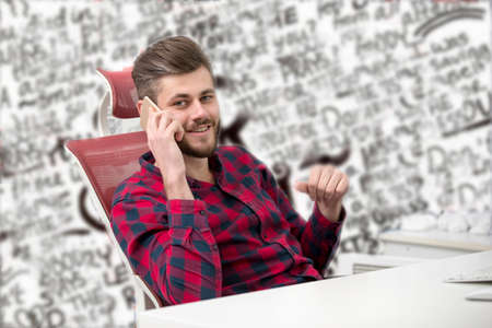 Handsome young man talking on phone while doing paperwork at workplace