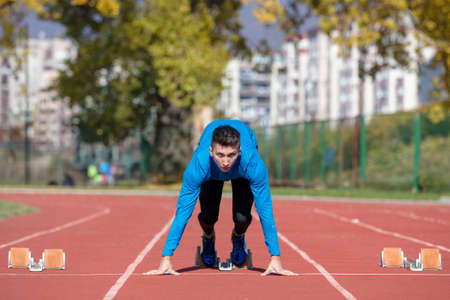 Man runner in blue shirt and shorts and sport shoes in steady position before run at start of race.の写真素材