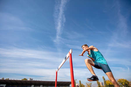 Low angle view of determined male athlete jumping over a hurdlesの写真素材