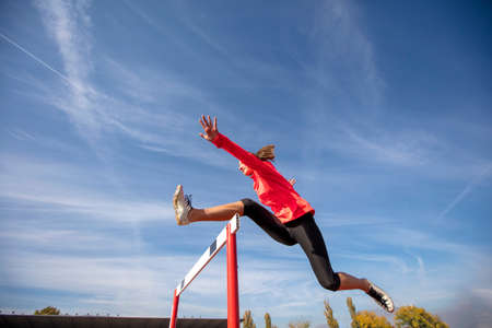 Female athlete jumping above the hurdle during the raceの写真素材