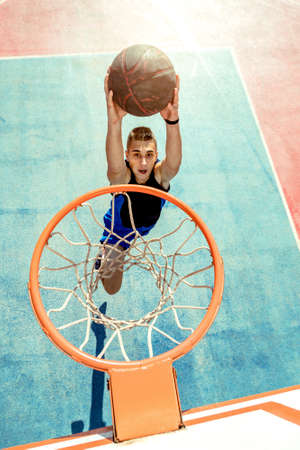 Young man jumping and making a fantastic slam dunk playing streetball, basketball. Urban authentic.