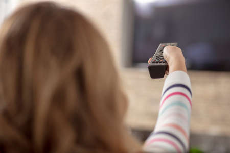 Beautiful woman lying on a sofa with remote control and watching television