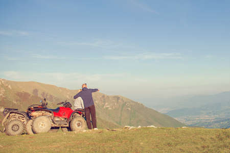 Rear view of young pair near atv. Man is showing something in distance to her girlfriend.