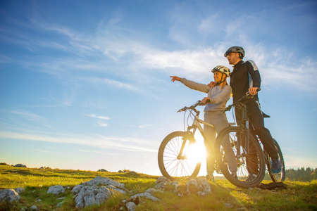 Biker couple with mountain bike pointing in distance at countrysideの写真素材