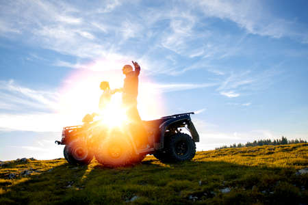 Beautiful couple is watching the sunset from the mountain sitting on atv quadbike