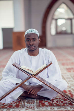 Black African Muslim Man Is Praying In The Mosque with open holy book of Koran