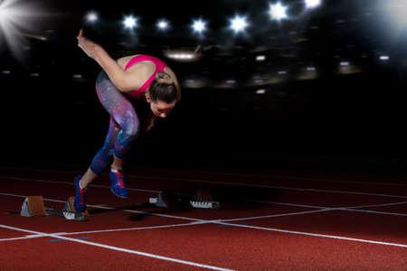 woman sprinter leaving starting blocks on the athletic track. exploding start on stadium with...