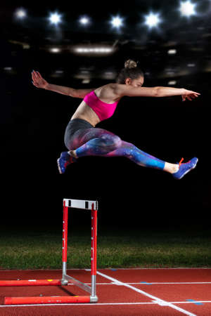 Determined young woman athlete jumping over a hurdlesの写真素材