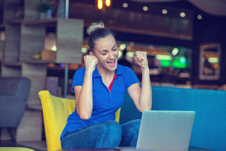 Winner girl euphoric watching a laptop in a coffee shop wearing a blue shirt