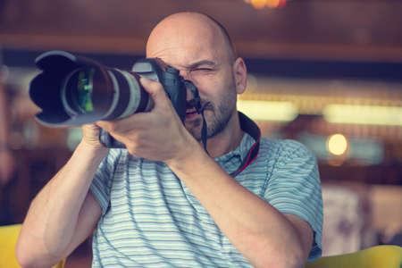 bald man holds a camera in his hands.