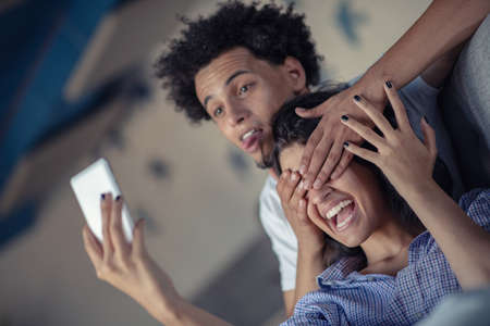 Attractive couple sitting on couch together looking at smartphone at home in the living roomの写真素材