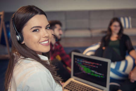 Portrait of businesswoman using laptop while colleague seen in background at creative office