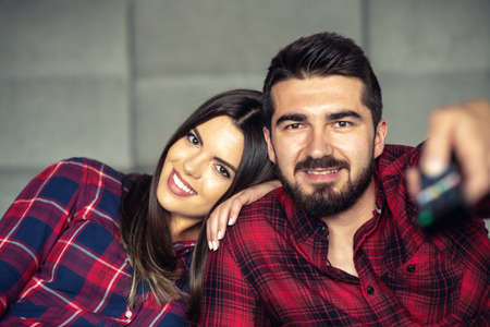 Couple fighting for remote control while watching TV at home