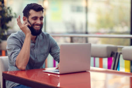 Half length portrait of successful bearded designer smiling at camera while working on freelance at netbook.の写真素材