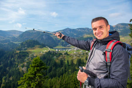Hiker young man with backpack and trekking poles standing on edge of cliff and looking at the lake, rear viewの写真素材