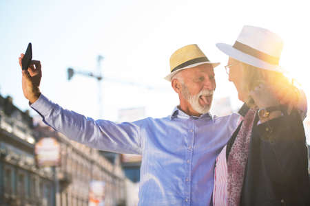 Tourism and technology. Traveling senior couple taking selfie together against sightseeing background.の写真素材