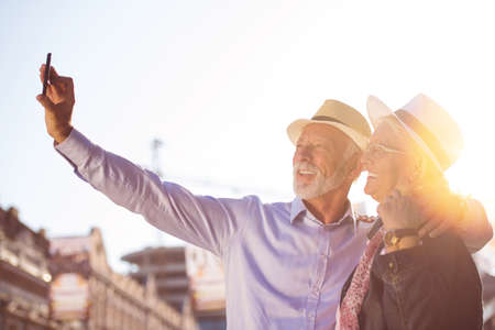 Tourism and technology. Traveling senior couple taking selfie together against sightseeing background.の写真素材