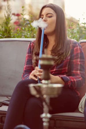 Young woman smoking a hookah outdoors. The pleasure of smoking. City in background