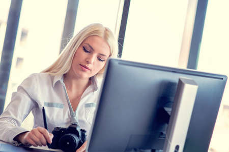 Professional photographer sitting at her office desk looking away and writing.の写真素材