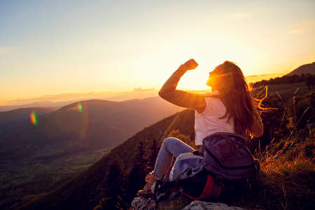Young woman rise hand up on top of mountain and sunset sky abstract backgroundの写真素材