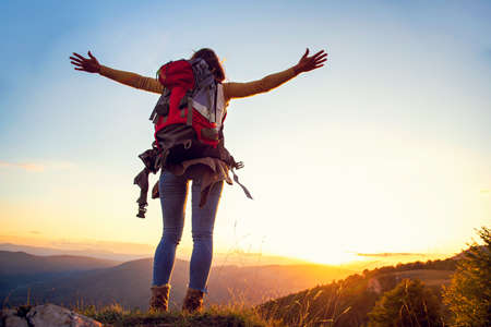 cheering woman hiker open arms at mountain peak.の写真素材