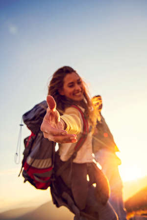 People helping each other hike up a mountain at sunrise.