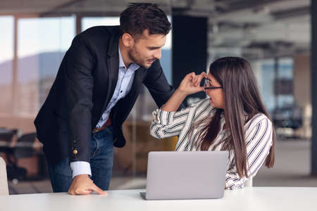 Couple of colleagues discussing work while sitting at the office and working on laptop.の写真素材