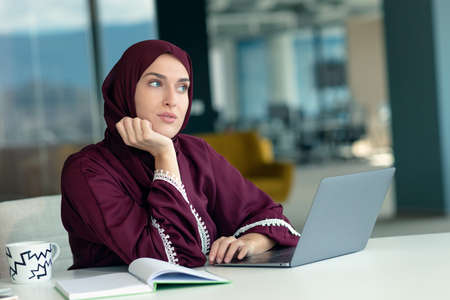 Pensive arabic businesswoman sitting at workplace in officeの写真素材