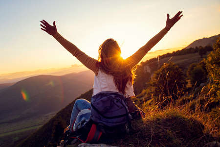 Young woman rise hand up on top of mountain and sunset sky abstract background