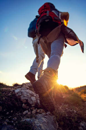 Tourist couple wearing hiking boots walk up a grassy hill in Alpsの写真素材