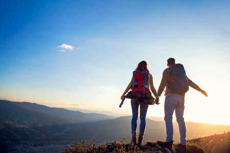 happy couple man and woman tourist at top of mountain at sunset outdoors during a hike in summer.の写真素材
