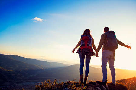 happy couple man and woman tourist at top of mountain at sunset outdoors during a hike in summer.の写真素材