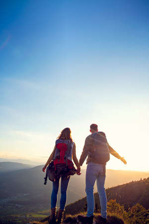 Hikers with backpacks relaxing on top of a mountain and enjoying the view of valley.の写真素材
