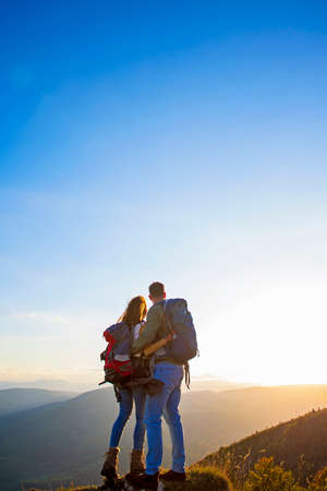 Hikers with backpacks relaxing on top of a mountain and enjoying the view of valley.の写真素材